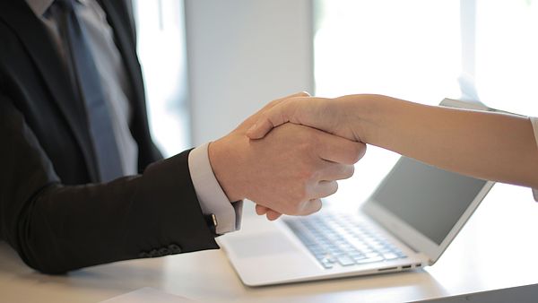Symbildbild zeigt Handschlag zweier Menschen in Bürosituation.