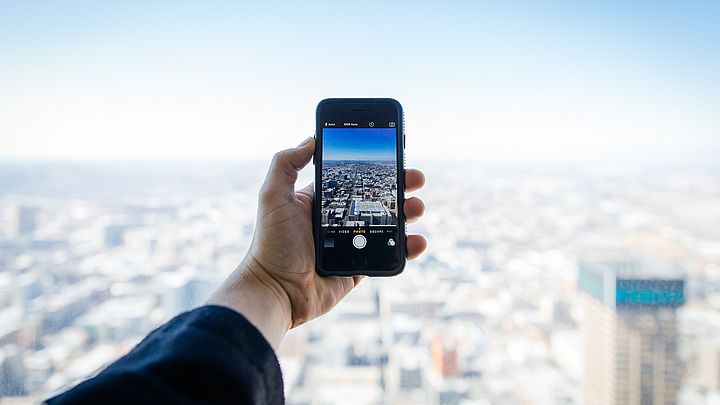 Person hält Smartphonebildschirm vor Stadtkulisse.